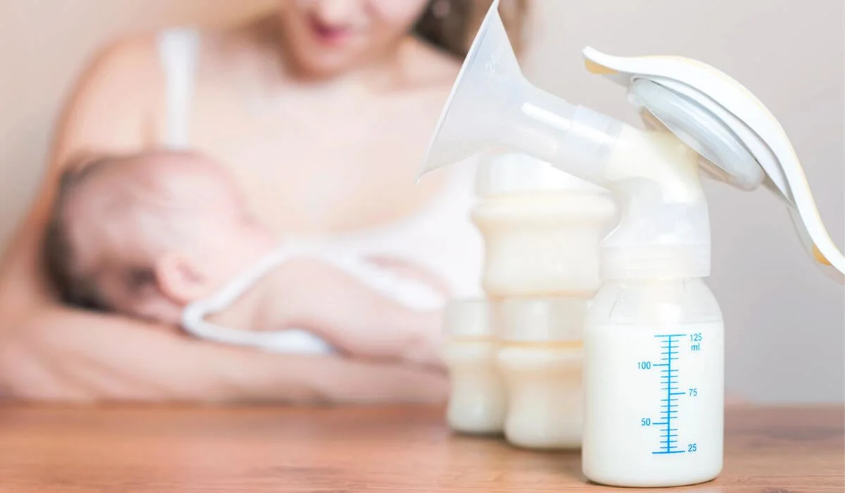 woman holding baby with breast pump and milk on table