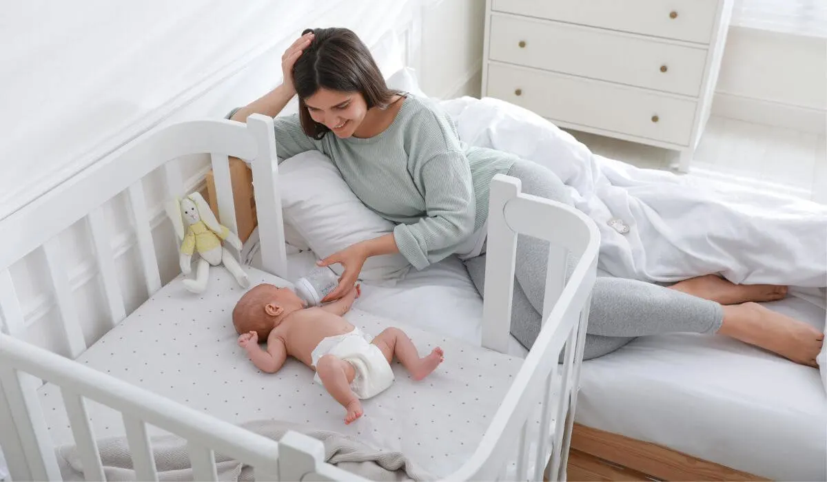Woman lying next to newborn in a co-sleeper cot