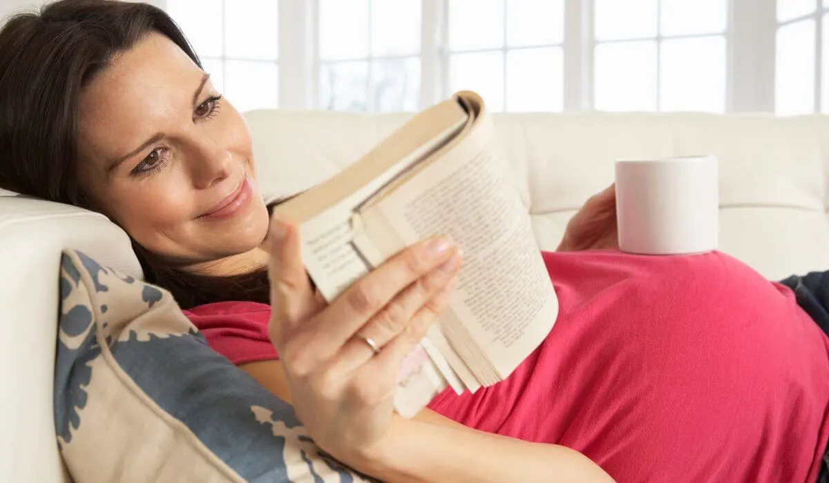 pregnant woman reading a book on the couch