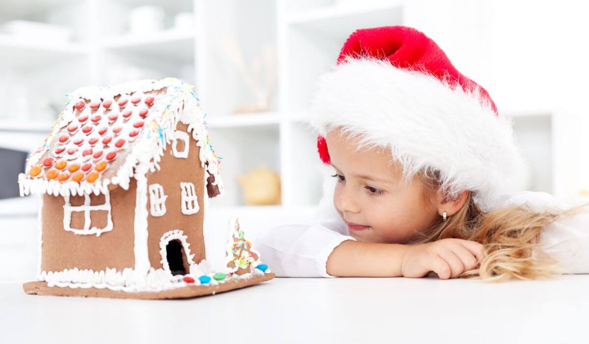 little girl with santa hat looking at gingerbread house
