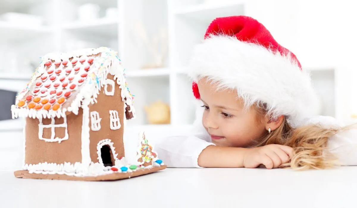 Little girl with santa hat looking at gingerbread house