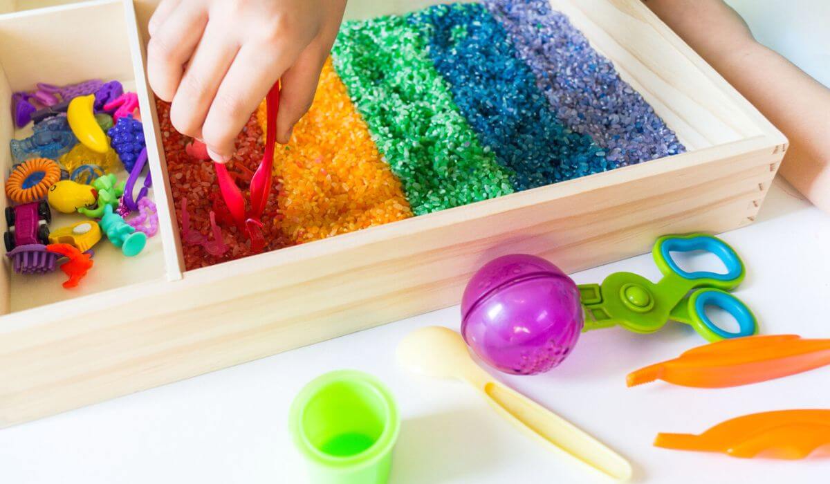 Sensory tray filled with rainbow rice and toys