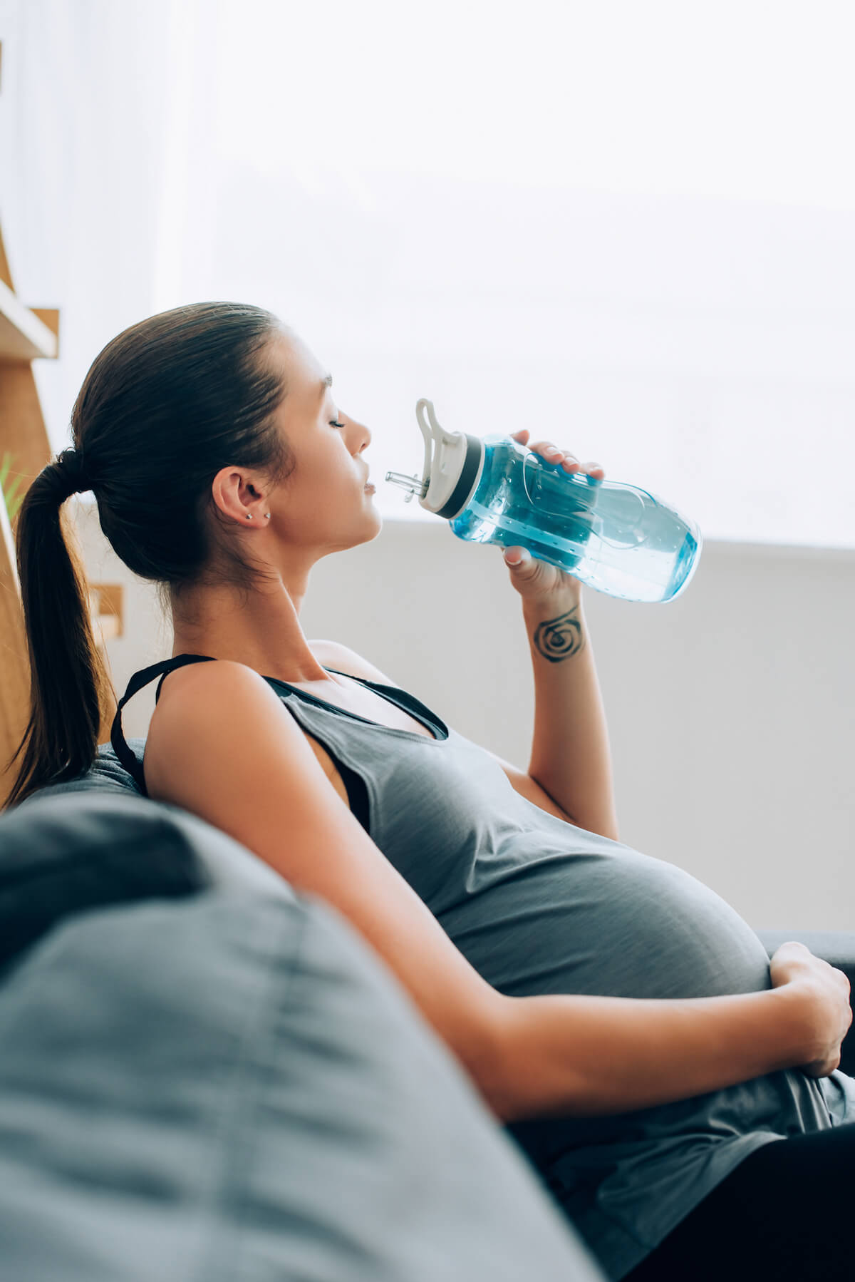 Pregnant woman on couch with water bottle