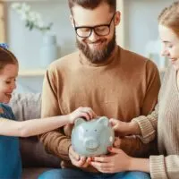 child with parents putting coin in piggy bank
