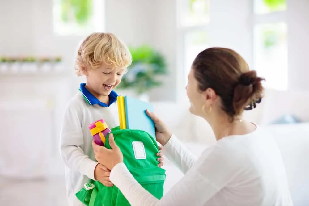 Mother helping son pack school back before starting school for the first time