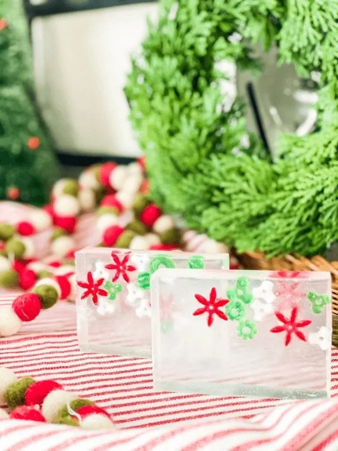 Homemade christmas soap bars sitting on a red and white cloth with a wreath in the background.