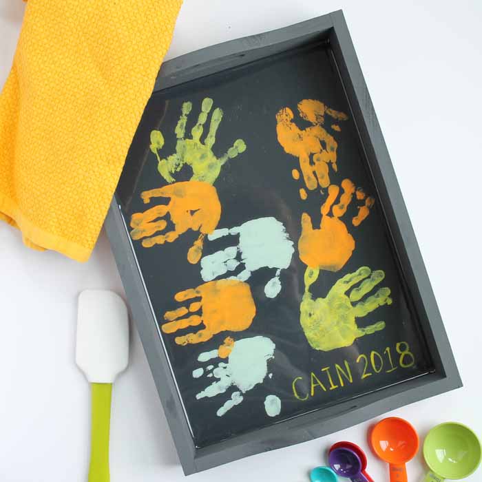Wooden tray deocrorated with children's handprints in orange, green and blue paint.