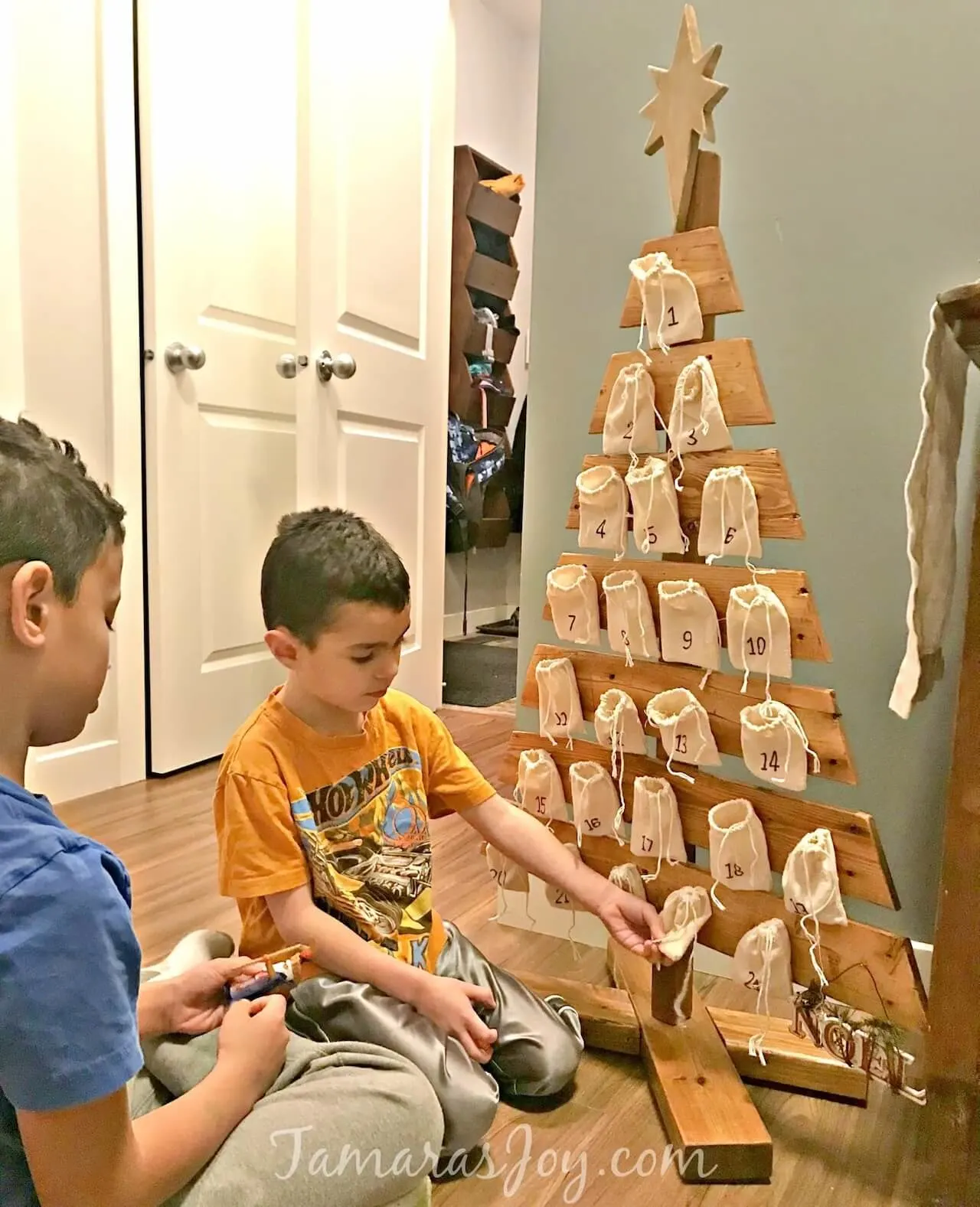 Wooden pallet advent tree with two little boys opening gifts.