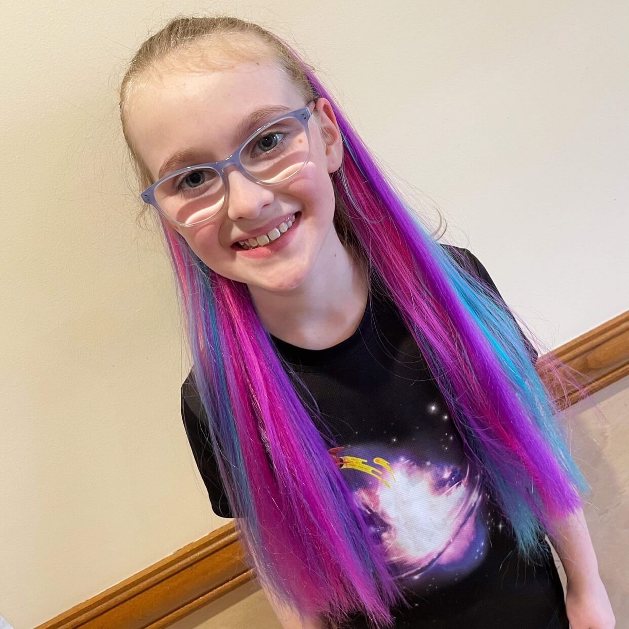 Rainbow hair extensions on a little girl with glasses.