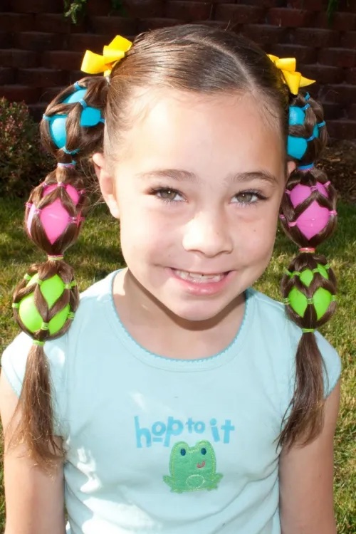 Little girl with long hair wearing plastic easter eggs inside her ponytail.