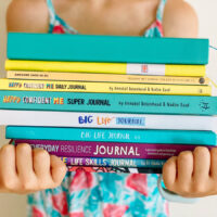 growth mindset and gratitude journals stacked in child's arms