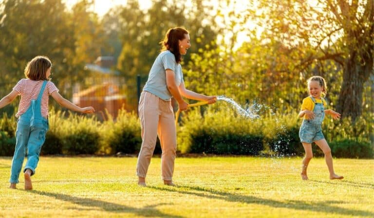 mother and two daughters playing under the hose in the backyard
