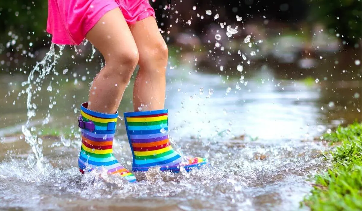Child with rainbow gumboots jumping in a puddle