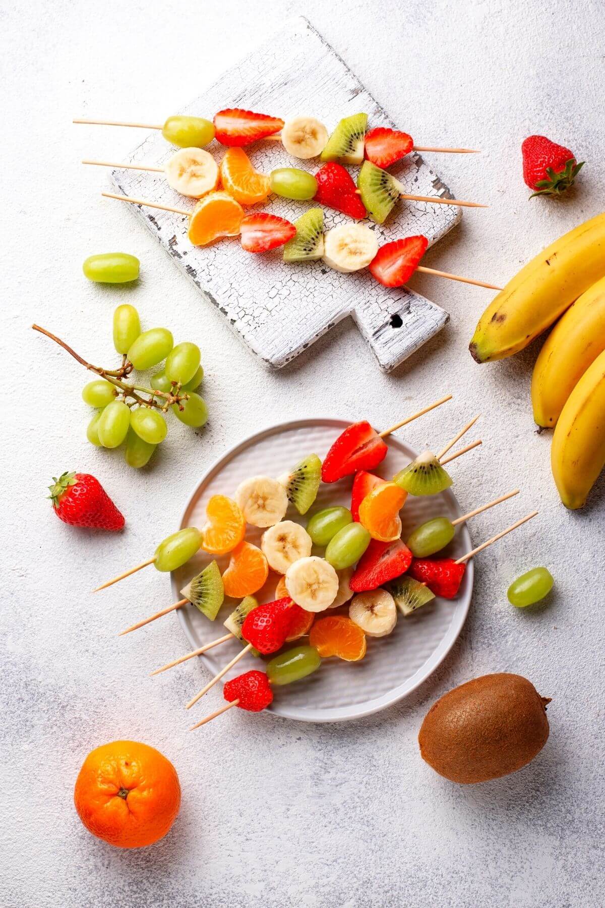 Fruit kabobs on a white plate with fruit scattered around