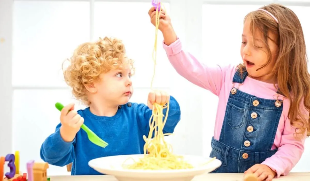 Two kids eating plain spaghetti from a bowl