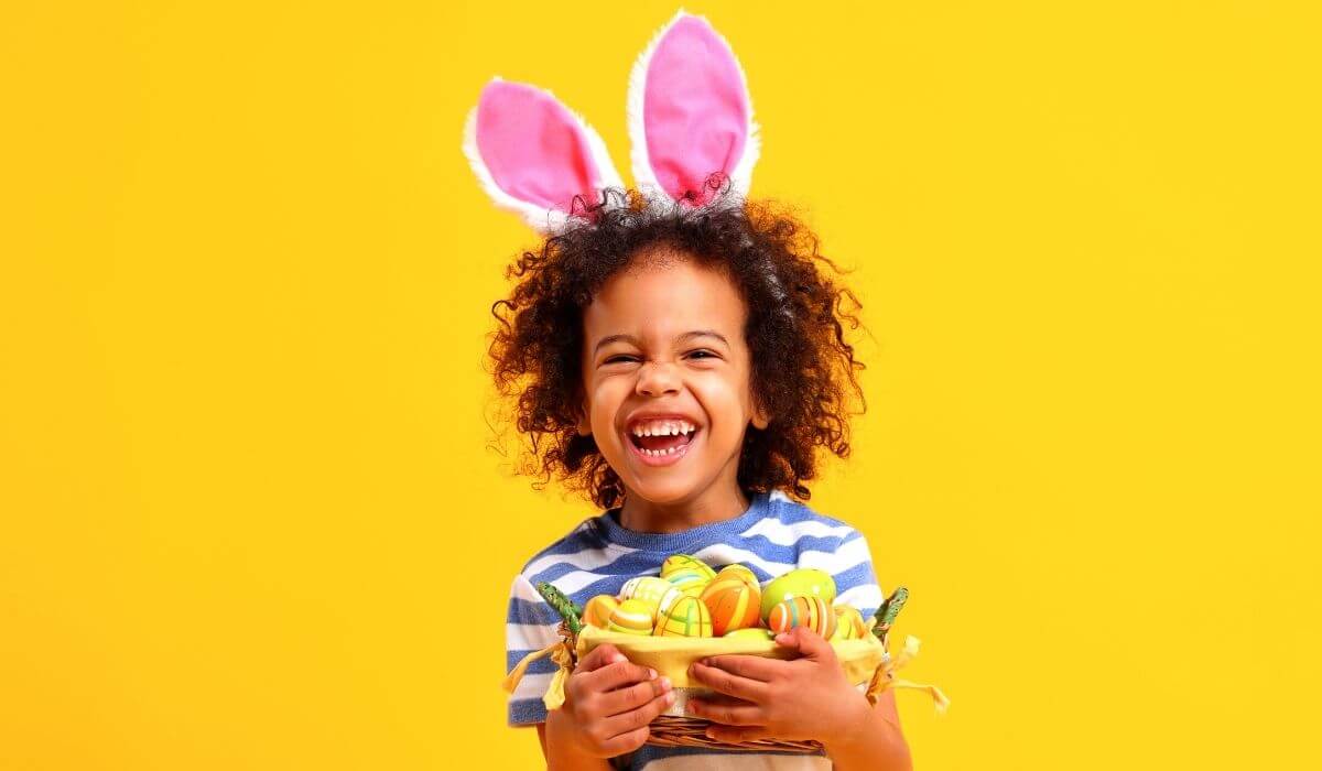 child with bunny ears and easter basket on yellow background
