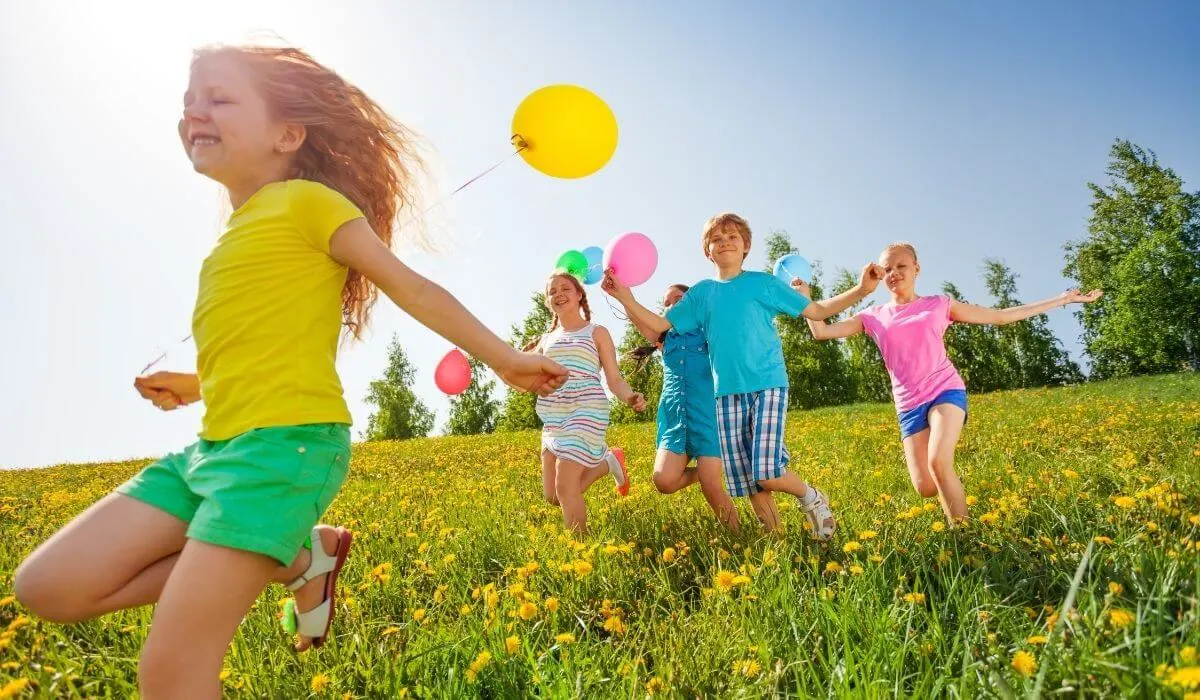 niños corriendo en la hierba con globos en cuerdas