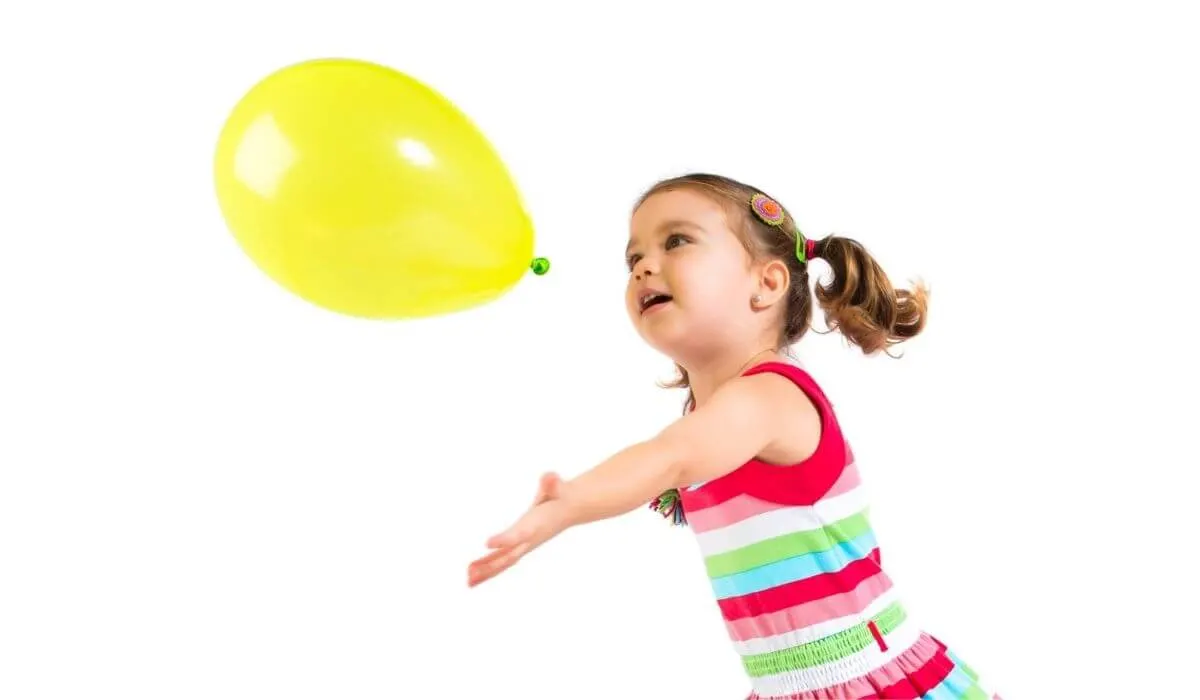 niña golpeando globo amarillo en el aire