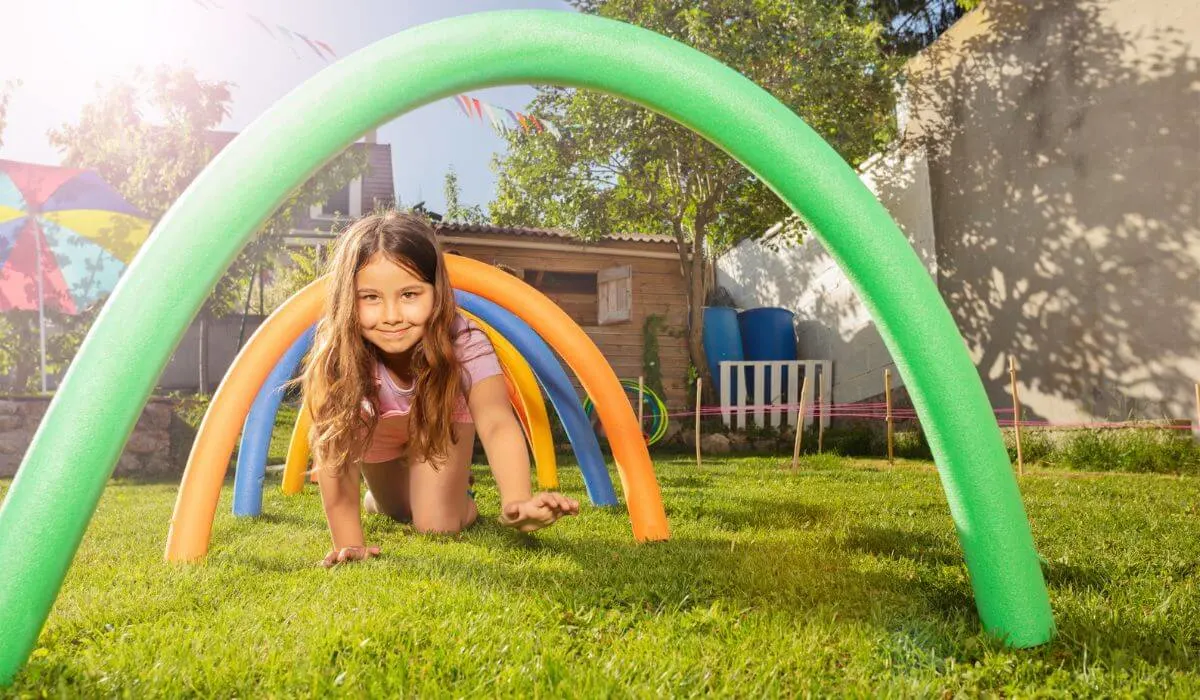 Young girl crawling under pool noodle tunnel