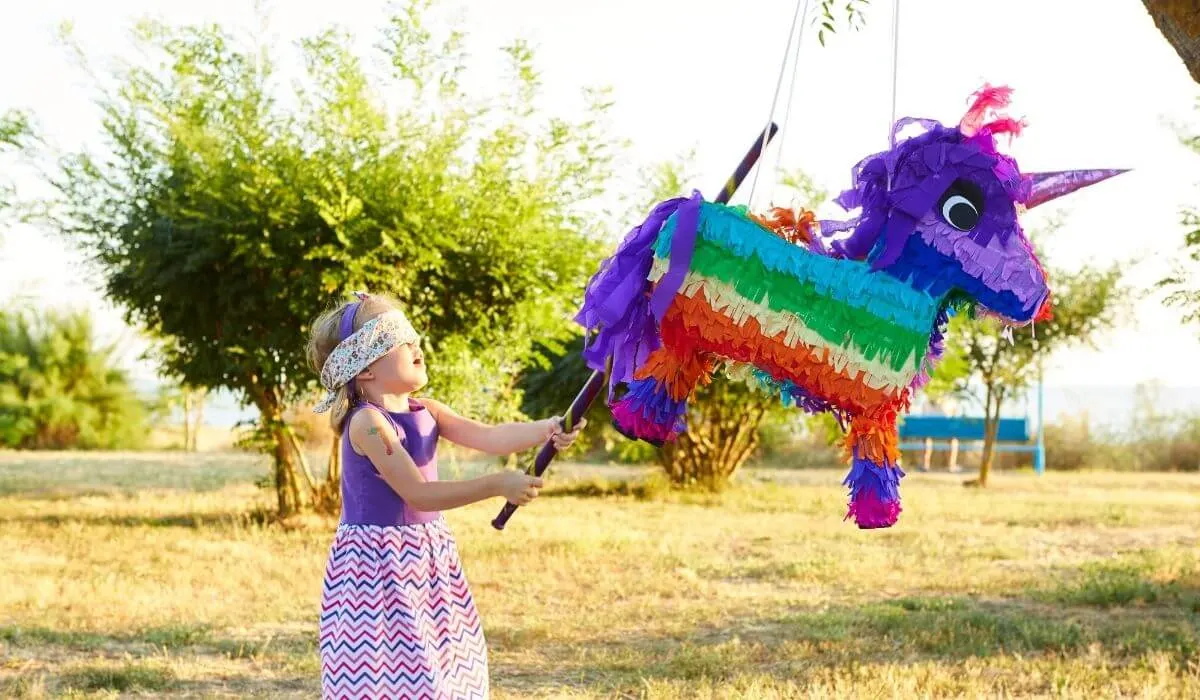 una niña golpeando una piñata de unicornio en una fiesta de cumpleaños