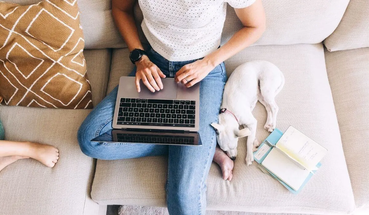 Woman working on laptop on her couch with her child and dog beside her