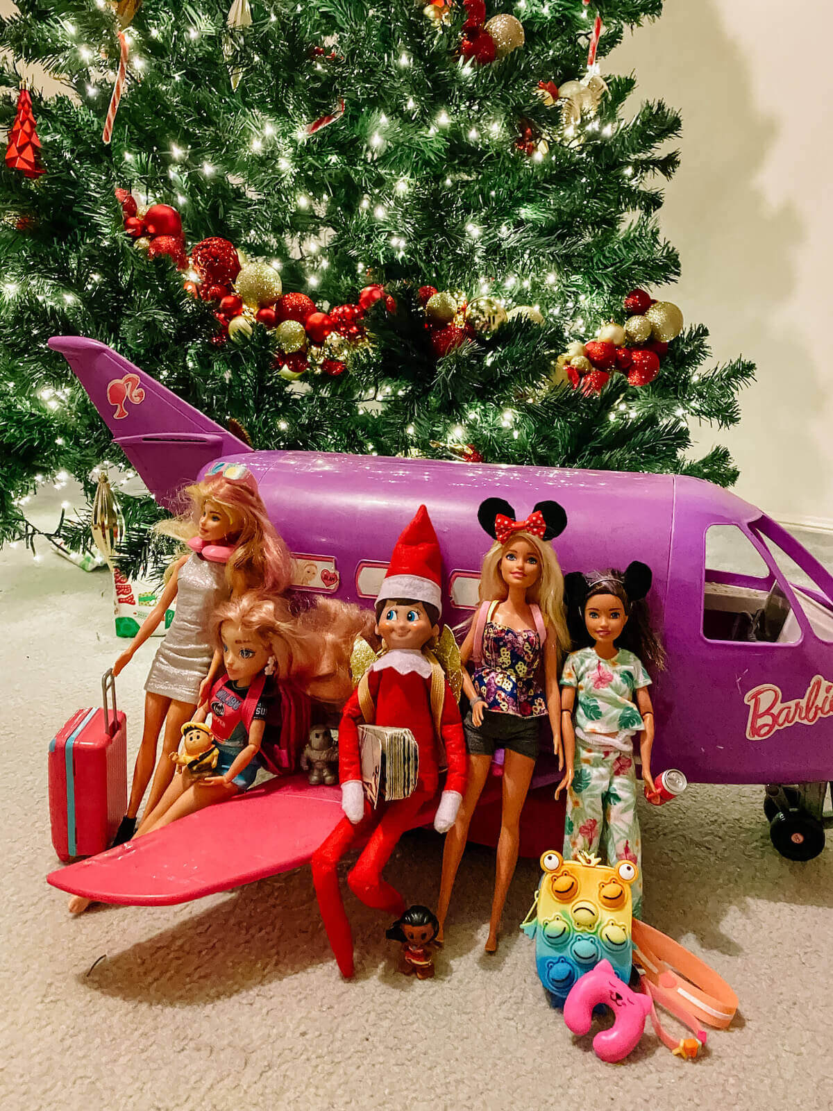 Elf on the shelf going on holidays with barbies in front of barbie plane
