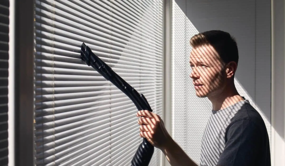 Man vacuuming vertical blinds on window