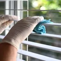 person wearing rubber gloves cleaning vertical blinds
