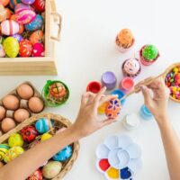 person decorating easter eggs with decorated eggs and paints on desk