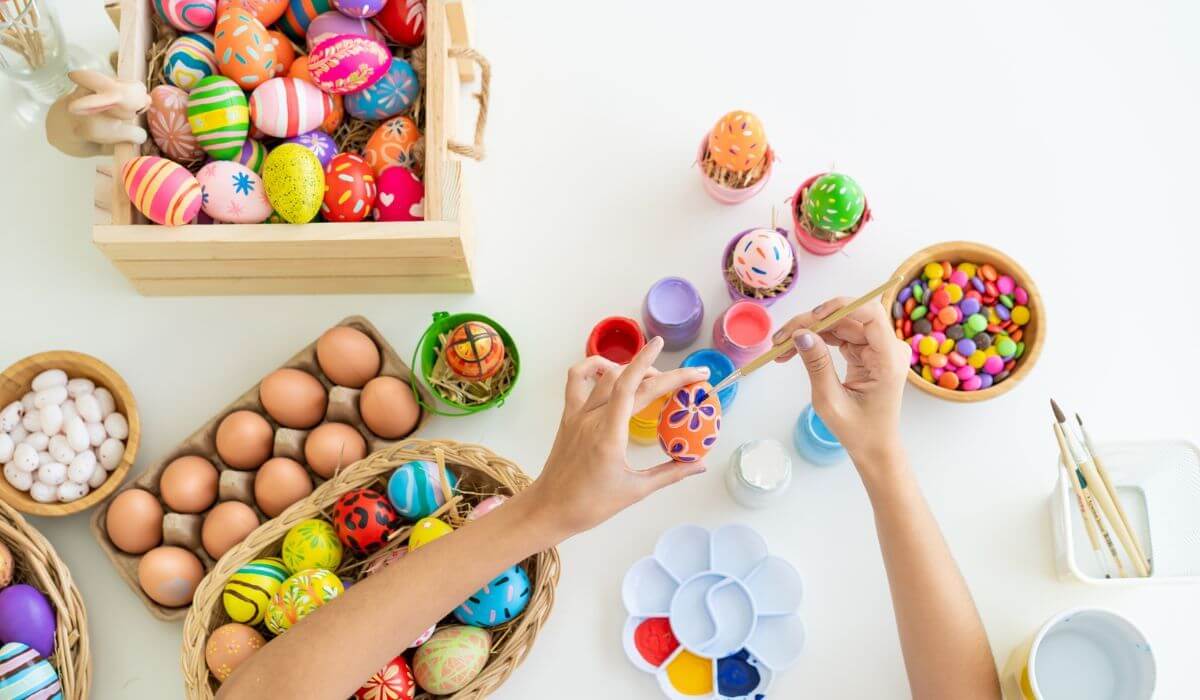 Person decorating easter eggs with decorated eggs and paints on desk
