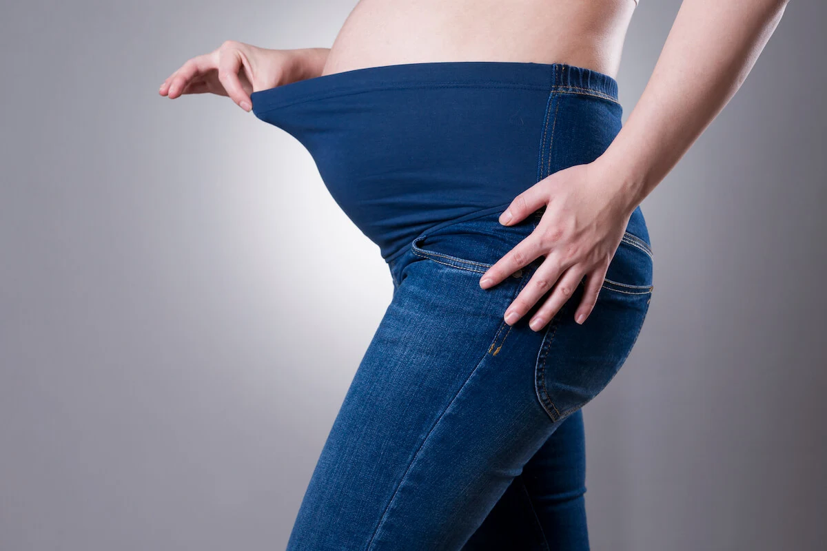 a woman wearing maternity jeans with a blue belly band