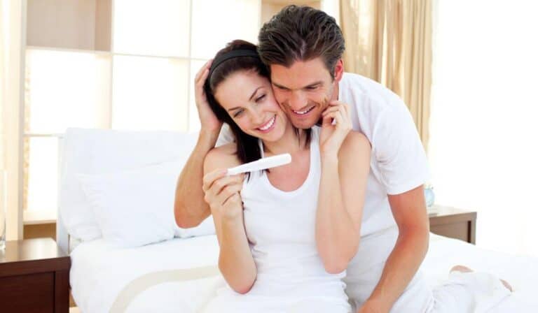 a couple excited looking at a positive pregnancy test while sitting on their bed