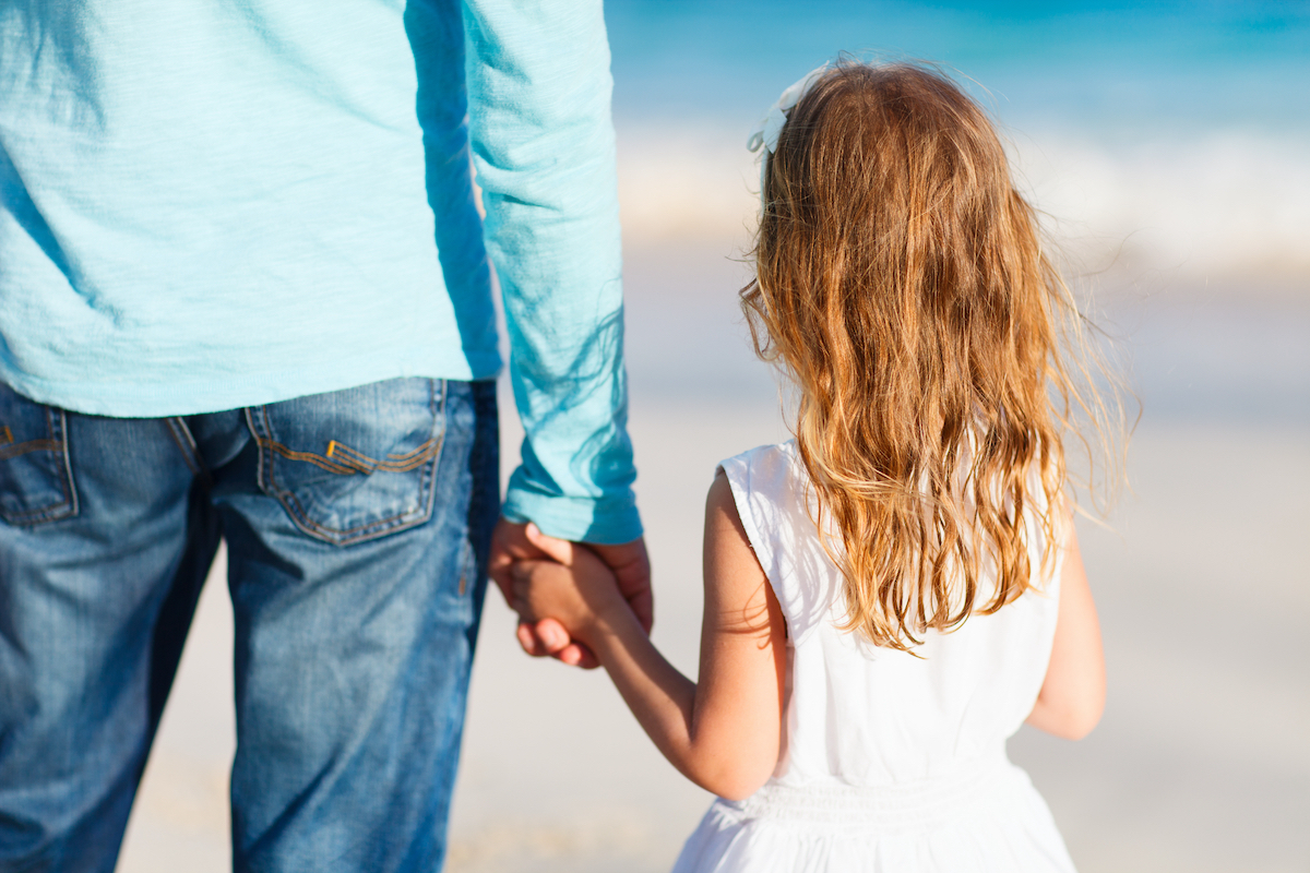 Adorable little girl holding her father hand on the beach