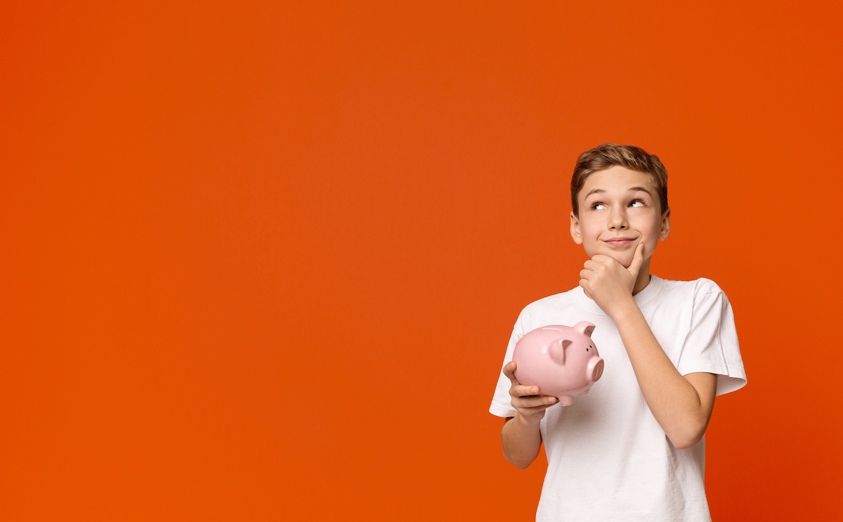 Teen boy with piggy bank dreaming about some things he can buy, orange studio background with empty space