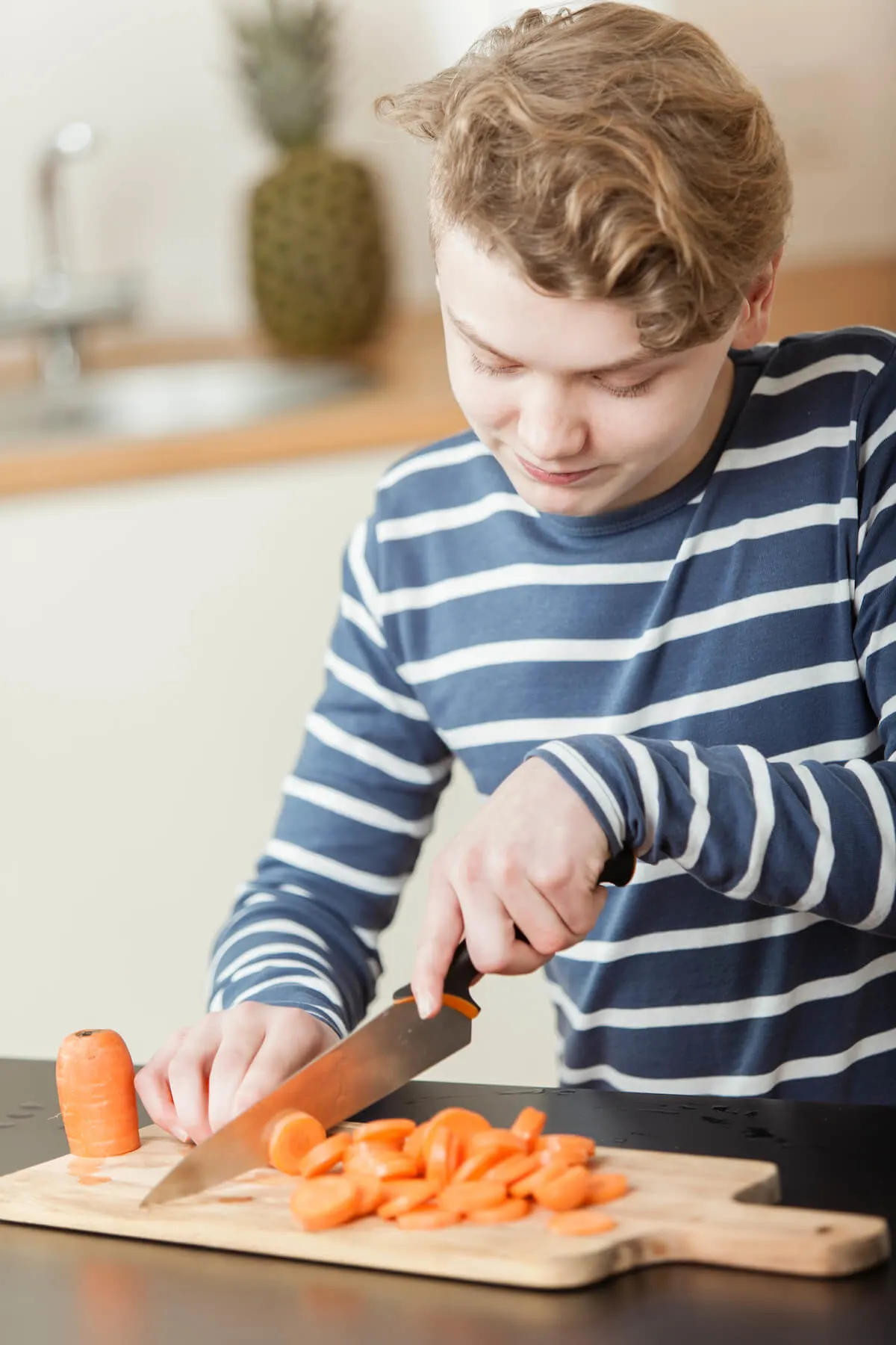Teenage boy in striped shirt cutting carrots on a chopping board