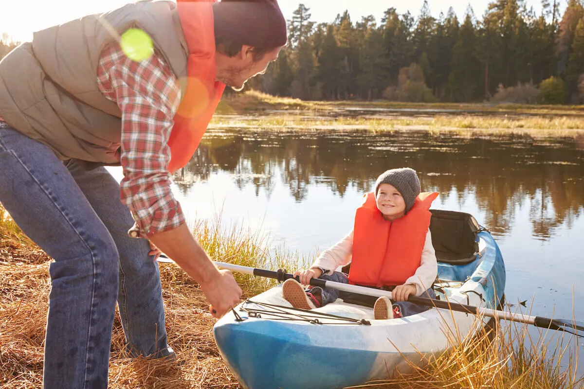 Father pushing blue kayak into water with young son sitting in kayak