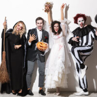 4 friends in fancy dress costumes at a halloween party including a witch, clown, bride and vampire