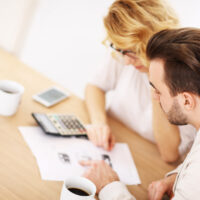 man and woman at dining table with calculator and paperwork preparing a household budget