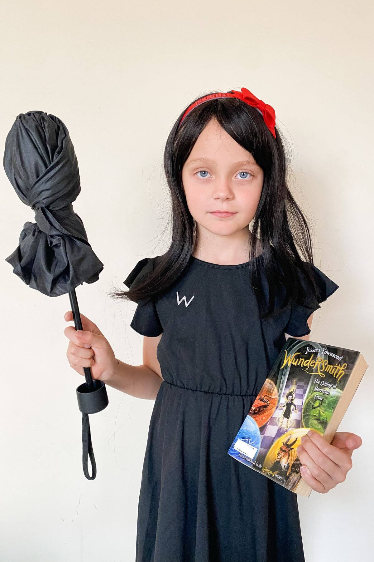 Child with serious face holding a black umbrella and a wundersmith: the trials of morrigan crow book in her hand