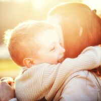 mother and son hugging outdoors with a sunflare