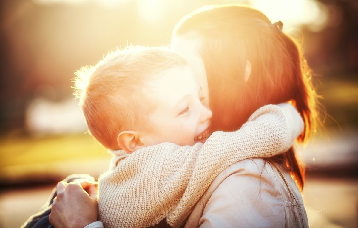 Mother and son hugging outdoors with a sunflare