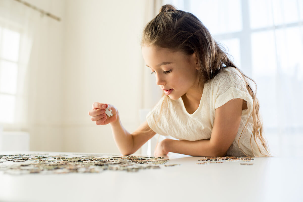 Little girl in white shirt sitting at a table doing a jigsaw puzzle