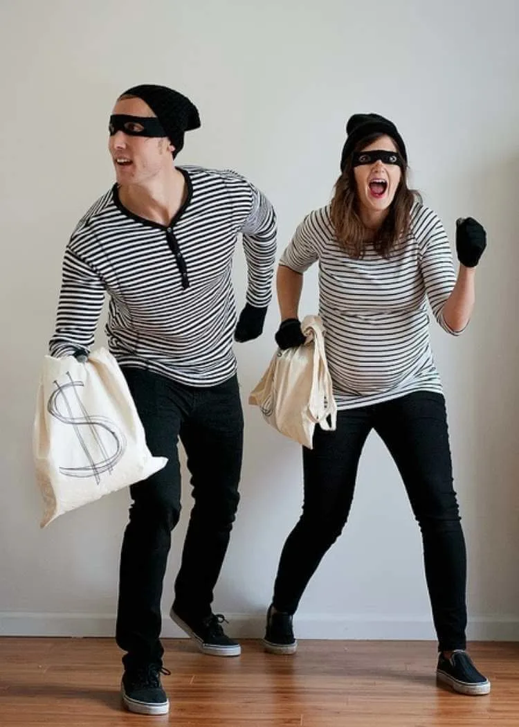 Man and woman dressed as bank robbers with masks and striped shirts holding money bags