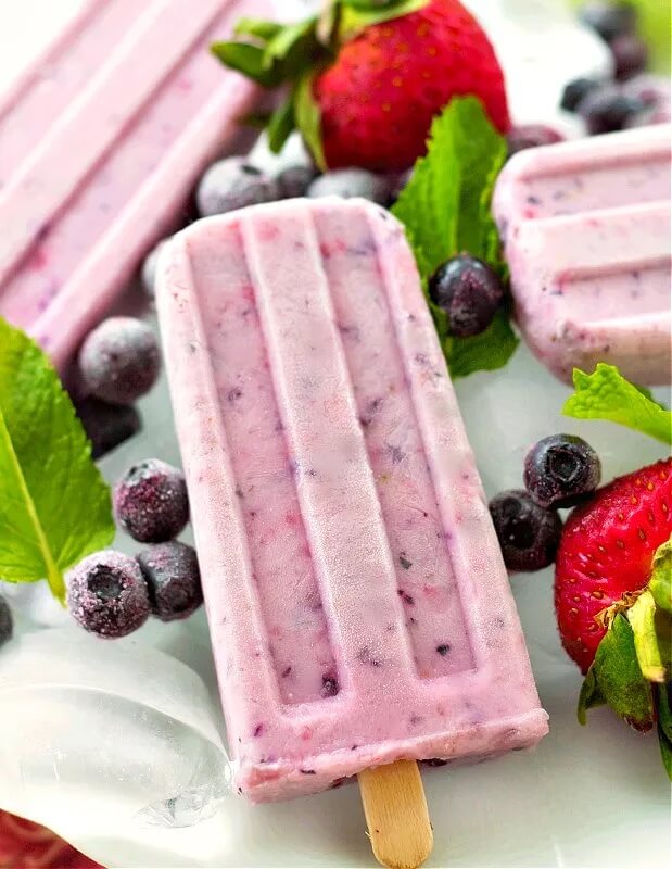 Three berry yogurt popsicles surrounded by fresh berries