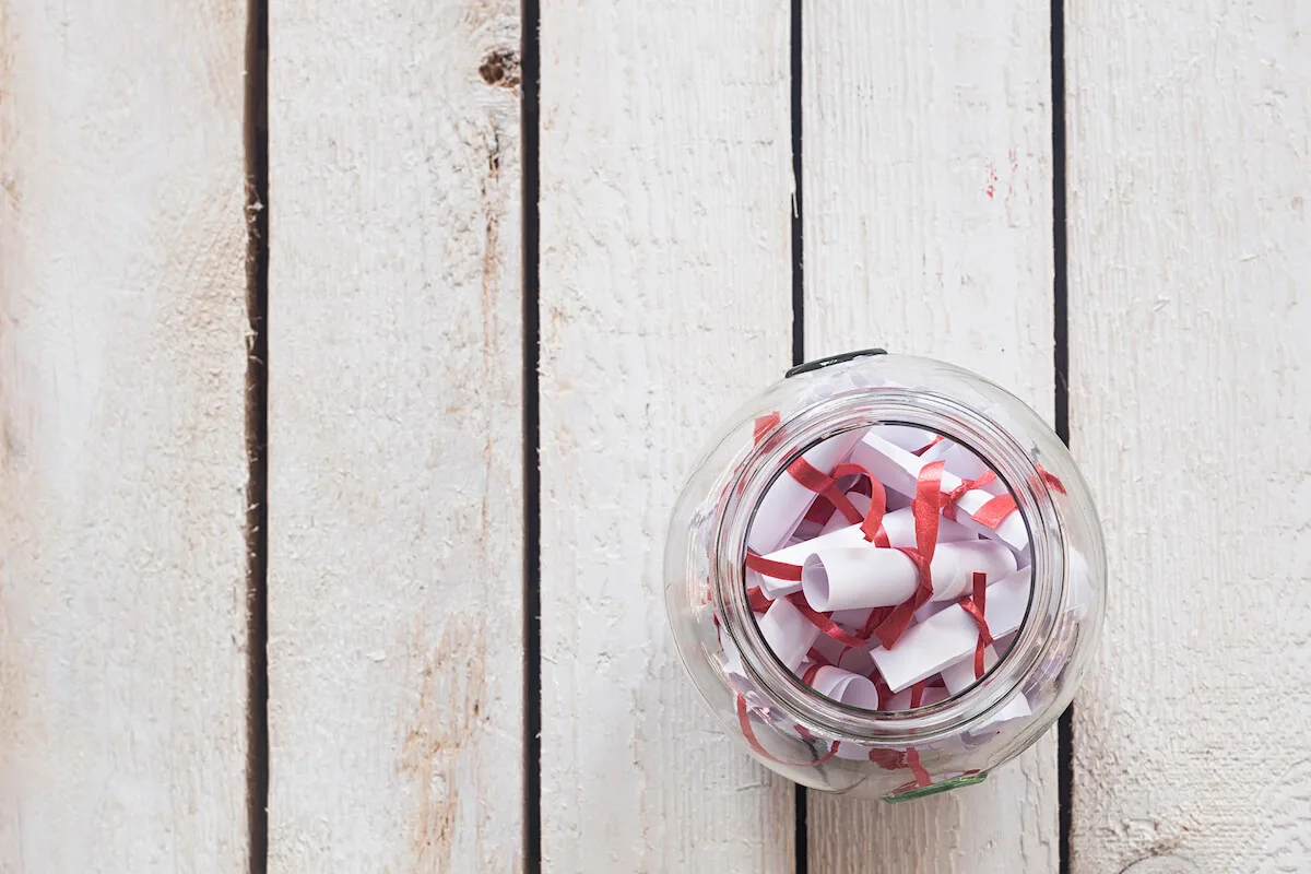 Diy date night jar with slips of paper tied with ribbon inside a glass jar