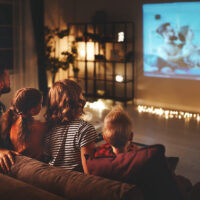family of 4 sitting on their couch with fairy lights on, watching a movie at home