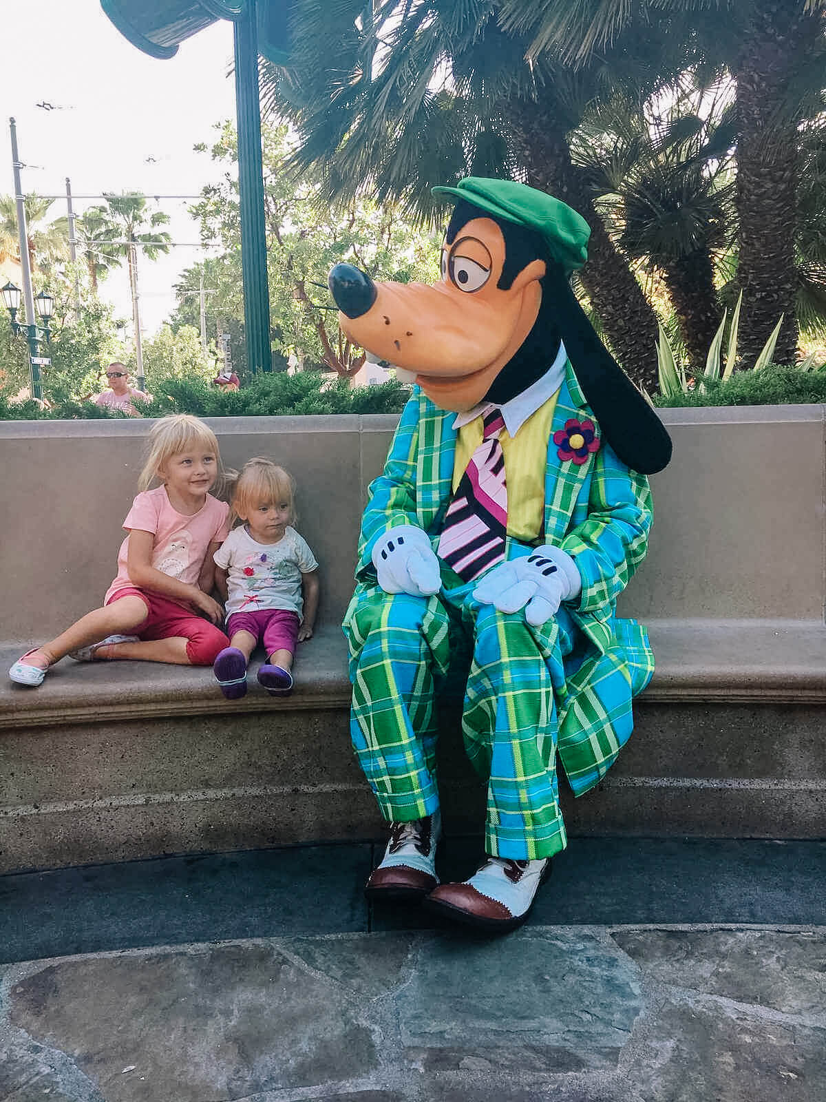Two young kids sitting next to goofy at disney california adventure park.
