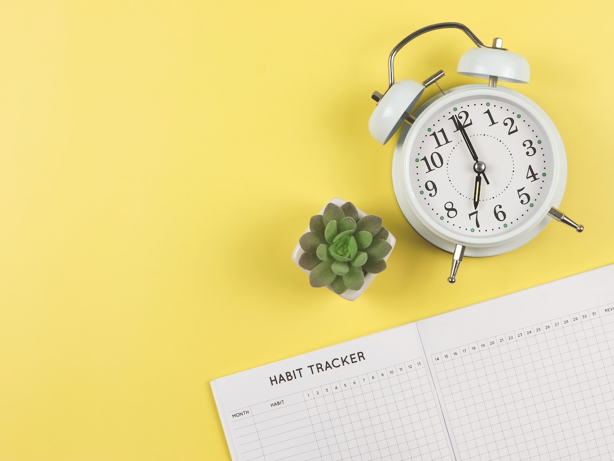 Top view or flat lay of habit tracker book, white vintage alarm clock and succulent plant pot on blue background with copy space.