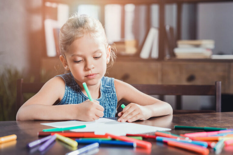 Young girl sitting at a desk with a sketch pad and coloured markers drawing.