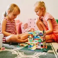 two young girls working together to build a rainbow coloured lego house.